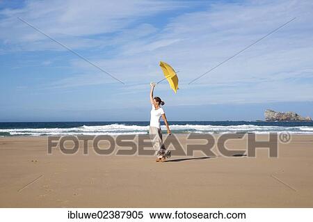 Woman walking with an umbrella on a windy beach View Large Photo Image Stock Photography - Woman walking with an umbrella on a windy beach. Fotosearch