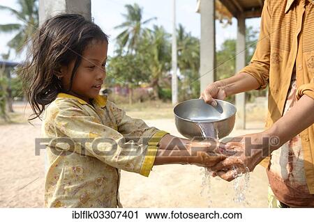 Stock Image - "Woman washing a girl's hands, hygiene education, Trapang Village, Bathi District, Takeo Province, Cambodia, Asia". Fotosearch