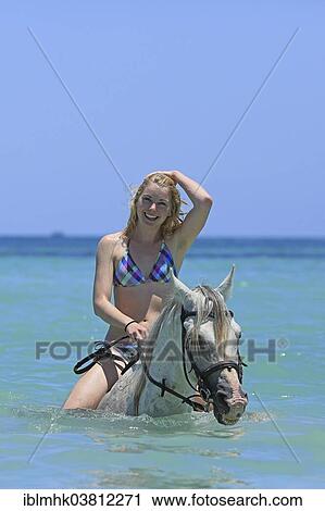 Stock Image - "Woman wearing a bikini riding a Barb horse in the sea, riding vacation, Djerba, Tunisia, Africa". Fotosearch