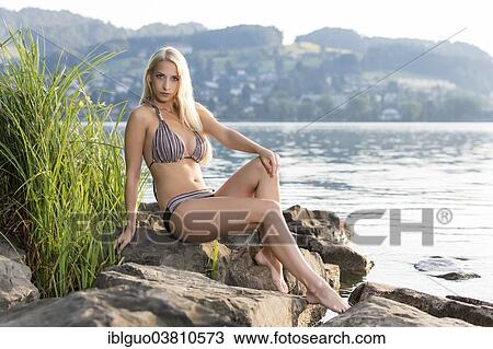 Woman wearing a bikini sitting on a rock by a lake View Large Photo Image Stock Image - Woman wearing a bikini sitting on a rock by a lake. Fotosearch