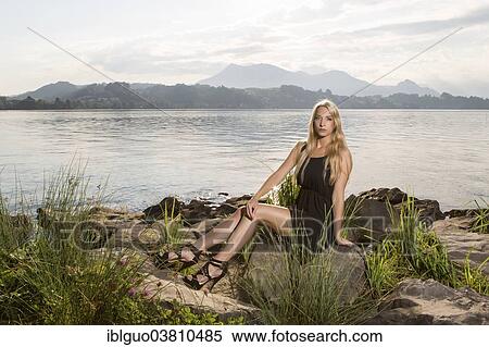 Woman wearing a black dress sitting on a lake shore View Large Photo Image Stock Photography - Woman wearing a black dress sitting on a lake shore. Fotosearch
