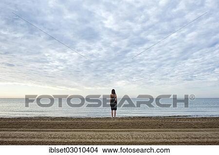 Picture - "Woman wearing a black dress standing by the sea, moody clouds, Cavallino, Jesolo, Venedig, Italy, Europe". Fotosearch