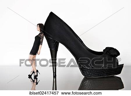 Woman wearing a black mini dress and high heels leaning against an oversized shoe, photomontage View Large Photo Image Stock Photo - Woman wearing a black mini dress and high heels leaning against an oversized shoe, photomontage. Fotosearch
