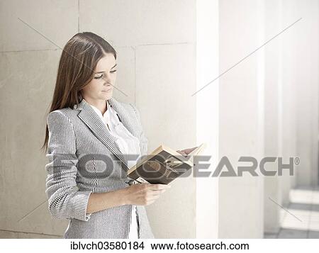 Picture - "Woman wearing a business suit leaning against a wall and reading a book, Innsbruck, Tyrol, Austria, Europe". Fotosearch