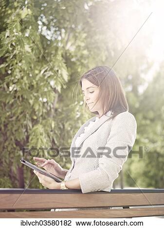 "Woman wearing a business suit standing with a tablet computer behind a park bench, Innsbruck, Tyrol, Austria, Europe" View Large Photo Image Stock Image - "Woman wearing a business suit standing with a tablet computer behind a park bench, Innsbruck, Tyrol, Austria, Europe". Fotosearch