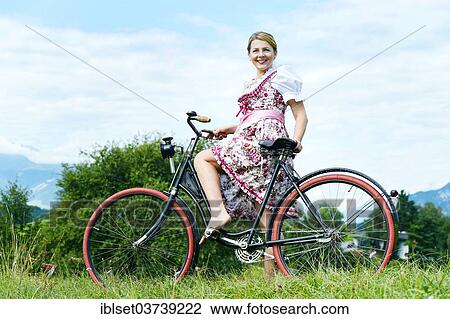 Stock Image - "Woman wearing a dirndl on an old bicycle, Igls, Innsbruck, Tyrol, Austria, Europe". Fotosearch
