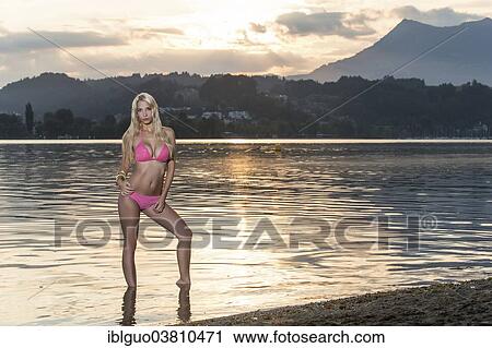 Woman wearing a pink bikini standing at a lakeside beach at sunrise View Large Photo Image Stock Image - Woman wearing a pink bikini standing at a lakeside beach at sunrise. Fotosearch