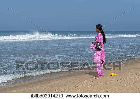 Stock Image - "Woman wearing a pink shalwar kameez standing on the beach facing the sea, Varkala, Kerala, India, Asia". Fotosearch