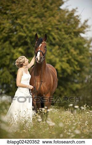Woman Wearing A Wedding Dress With A Hanoverian Horse In A Meadow