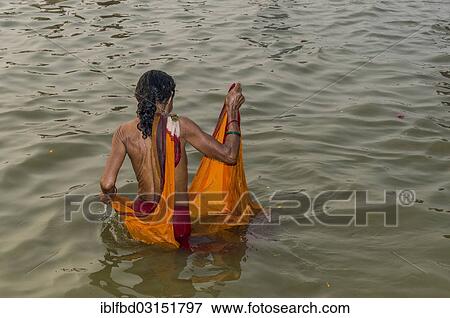 Stock Photo - "Woman wearing an orange sari taking a bath in the Sangam, the confluence of the rivers Ganges, Yamuna and Saraswati, in the early morning, Kumbha Mela mass Hindu pilgrimage, Allahabad, Uttar Pradesh, India, Asia". Fotosearch