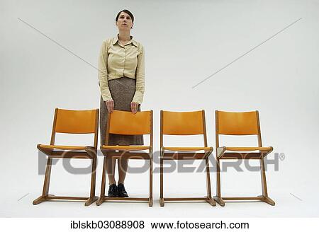 Stock Photo - Woman wearing conservative clothes standing behind a row of orange chairs. Fotosearch
