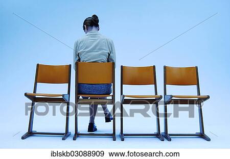 Stock Photo - "Woman wearing conservative clothes sitting on one of four orange chairs, rear view". Fotosearch