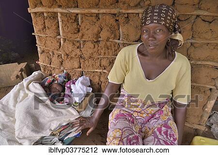 Stock Image - "Woman with a child sitting in front of her hut, near Kent, Western Area Region, Sierra Leone, Africa". Fotosearch