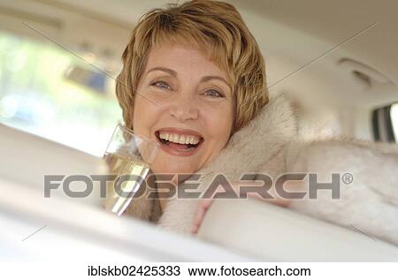 "Woman with a fur coat sitting in a car holding a glass of champagne, portrait" View Large Photo Image Stock Image - "Woman with a fur coat sitting in a car holding a glass of champagne, portrait". Fotosearch