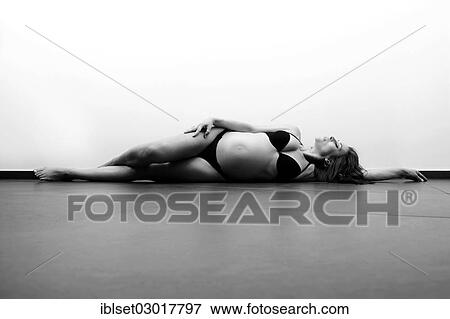 Stock Photo - Woman with a pregnant belly lying on the floor in underwear. Fotosearch