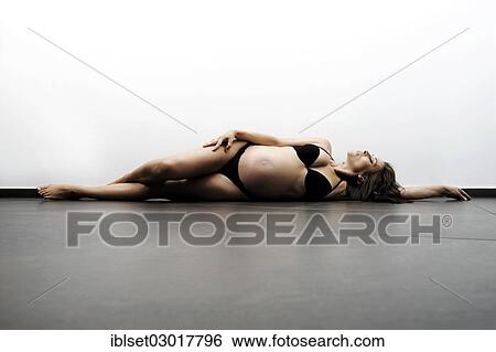 Stock Photograph - Woman with a pregnant belly lying on the floor in underwear. Fotosearch