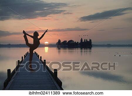 "Woman with backlighting doing a yoga pose on a wooden pier at a lake in front of the setting sun, Steinhude am Meer, Lower Saxony, Germany, Europe" View Large Photo Image Stock Photo - "Woman with backlighting doing a yoga pose on a wooden pier at a lake in front of the setting sun, Steinhude am Meer, Lower Saxony, Germany, Europe". Fotosearch