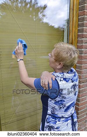 Picture - Woman with joint pain in her shoulder cleaning a window. Fotosearch
