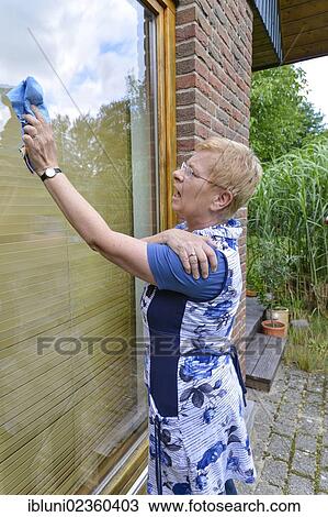 Stock Image - Woman with joint pain in her shoulder cleaning a window. Fotosearch