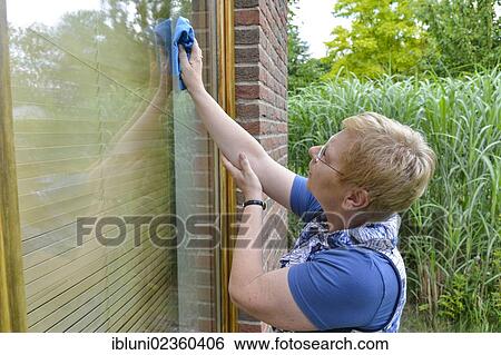 Stock Photograph - Woman with joint pain in her shoulder cleaning a window. Fotosearch