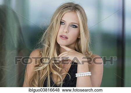 Stock Photo - "Woman with long blond hair leaning against a glass wall, thoughtful expression". Fotosearch
