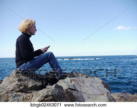"Woman with phone sitting on a rock and looking over the sea, in the Roque de las Bodegas, Tenerife, Canary Islands, Spain, Europe" View Large Photo Image Stock Image - "Woman with phone sitting on a rock and looking over the sea, in the Roque de las Bodegas, Tenerife, Canary Islands, Spain, Europe". Fotosearch