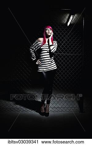Stock Image - Woman with pink hair in front of a chain link fence. Fotosearch