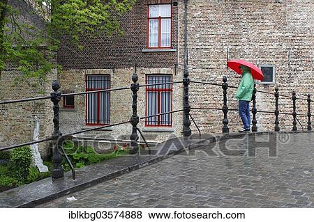 Stock Photo - "Woman with red umbrella in rain on bridge at Begijnhof nunnery, Bruges, West Flanders, Flemish Region, Belgium, Europe". Fotosearch