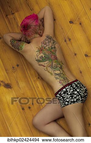Woman with tattoos on arm and back, skulls, flowers, phoenix, lying on the ground View Large Photo Image Picture - Woman with tattoos on arm and back, skulls, flowers, phoenix, lying on the ground. Fotosearch