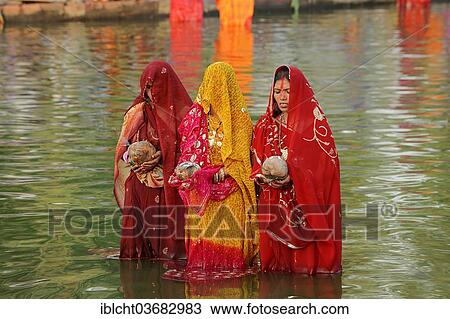 Stock Image - "Women wearing saris with offerings standing in water during the Hindu Chhath Festival, New Delhi, Delhi, India, Asia". Fotosearch