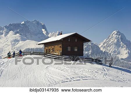 Stock Photography - "Wooden house on a snow-covered hill, Mt Alpspitze and Mt Zugspitze at back, Eckbauer, Garmisch-Partenkirchen, Upper Bavaria, Bavaria, Germany, Europe". Fotosearch