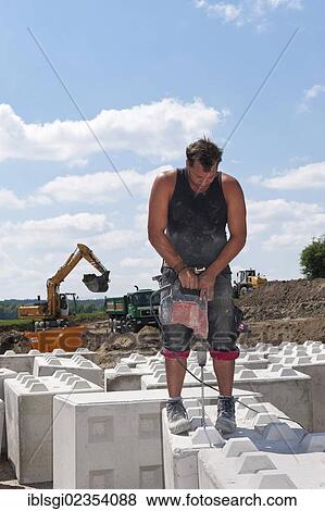 "Worker drilling holes into stone blocks that are to be used at a building site load test at a construction site in Fridolfing, Bavaria, Germany, Europe" View Large Photo Image Stock Photo - "Worker drilling holes into stone blocks that are to be used at a building site load test at a construction site in Fridolfing, Bavaria, Germany, Europe". Fotosearch