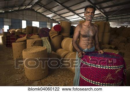 Stock Image - "Worker with rolled coconut fibre mats or coir mats, coconut fibre industry, factory, Alappuzha, Kerala, India, Asia". Fotosearch