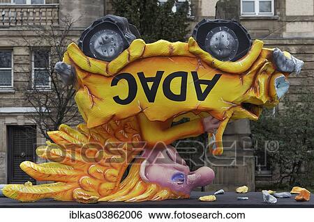 Stock Photograph - "Yellow angel in a car standing on its head, political caricature about the ADAC crisis, papier-mache figure for the Rose Monday parade, Carnival, Dusseldorf, North Rhine-Westphalia, Germany, Europe". Fotosearch