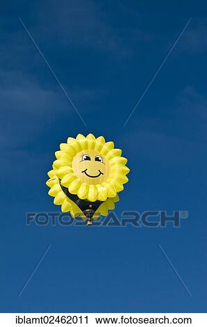 Stock Image - "Yellow balloon with a """"smiling sun"""" or sunflower face against a blue sky, 12th Tegernsee Montgolfiade 2012, balloon festival, Bad Wiessee, Tegernsee, Bavaria, Germany, Europe". Fotosearch