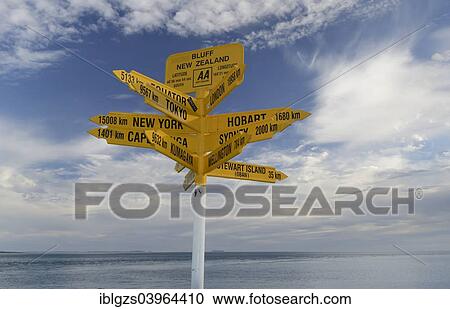 Stock Image - "Yellow signposts with worldwide destinations, the sea at the back, Bluff, South Island, New Zealand, Oceania". Fotosearch