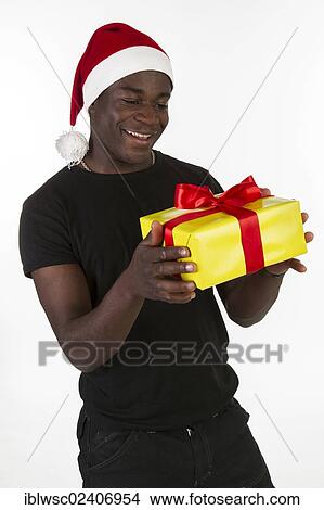 Picture - Young black man wearing a Santa hat and holding a present. Fotosearch