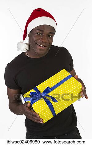 Stock Image - Young black man wearing a Santa hat and holding a present. Fotosearch