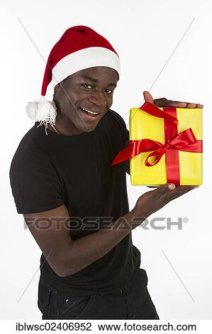 Stock Image - Young black man wearing a Santa hat and holding a present. Fotosearch