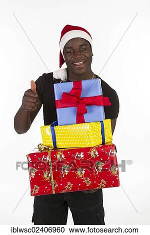 Stock Image - Young black man wearing a Santa hat and holding presents. Fotosearch