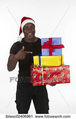 Stock Image - Young black man wearing a Santa hat and holding presents. Fotosearch