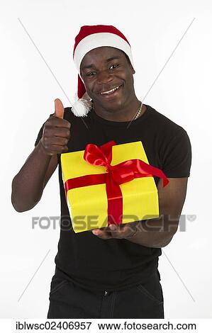 Stock Photo - "Young black man wearing a Santa hat and holding a present, thumbs up". Fotosearch