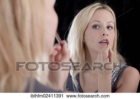 "Young blonde woman applying lipstick in front of a mirror, make-up" View Large Photo Image Stock Image - "Young blonde woman applying lipstick in front of a mirror, make-up". Fotosearch