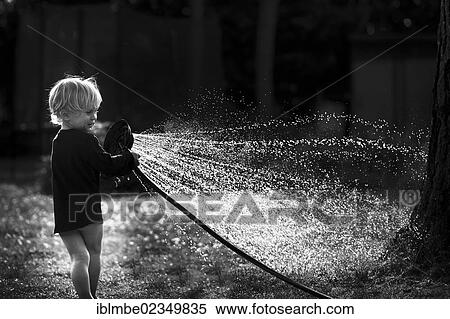 Stock Photography - "Young boy playing with a watering hose in a garden, with backlighting, Berlin, Berlin, Deutschland". Fotosearch