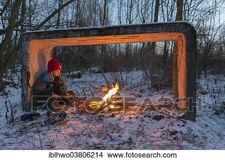 Picture - "Young boy sitting by the campfire in the snow toasting bread, Ettersberg ridge, Weimar, Thuringia, Germany, Europe". Fotosearch