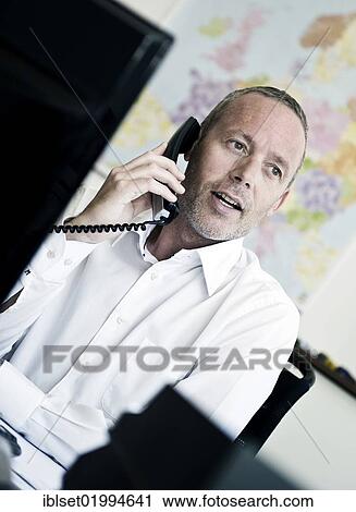 Stock Image - Young business man in an office talking on the telphone in front of a map of the world. Fotosearch