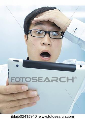 Stock Image - Young businessman, Asian, with glasses, iPad, amazed, surprised, shocked, stressed out. Fotosearch