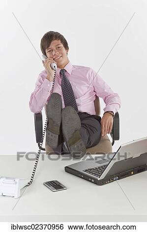 Young businessman talking on the phone in the office View Large Photo Image Stock Photograph - Young businessman talking on the phone in the office. Fotosearch