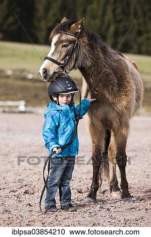 "Young child wearing a riding helmet standing beside a pony, dun, with a bridle, Tyrol, Austria, Europe" View Large Photo Image Stock Image - "Young child wearing a riding helmet standing beside a pony, dun, with a bridle, Tyrol, Austria, Europe". Fotosearch