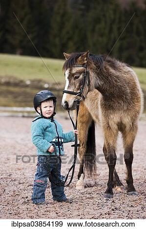 "Young child wearing a riding helmet holding a pony, dun, with a bridle, Tyrol, Austria, Europe" View Large Photo Image Stock Photo - "Young child wearing a riding helmet holding a pony, dun, with a bridle, Tyrol, Austria, Europe". Fotosearch